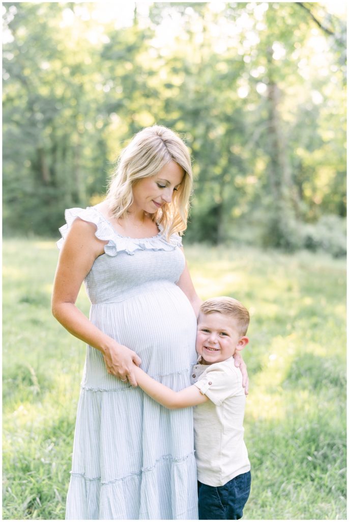 A pregnant mother looks down at her growing belly as her son hugs her and smiles. Atlanta Maternity Photographer Emily Grace Photography.