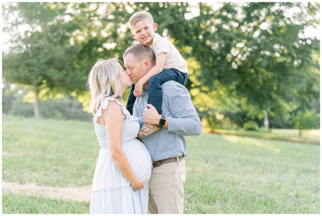 A pregnant mother and father kiss, with a smiling son on their shoulders. Grace Emily Photography, Atlanta Maternity Photographer, shares how to involve siblings in maternity photos.