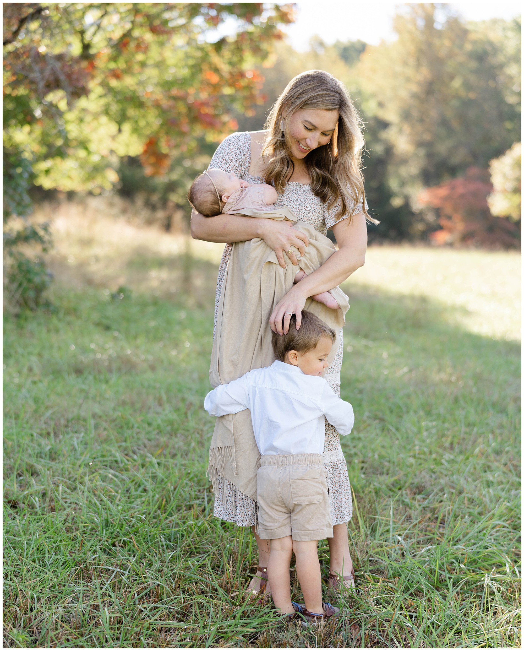 Mother holding her baby while her toddler son hugs her legs during fall family photos in Dahlonega.