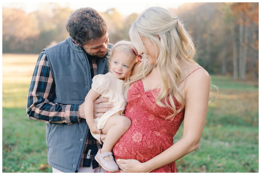 Atlanta fall mini session of expecting mother in a field of green grass lines by trees with yellow, red, and orange foliage by Grace Emily Photography.