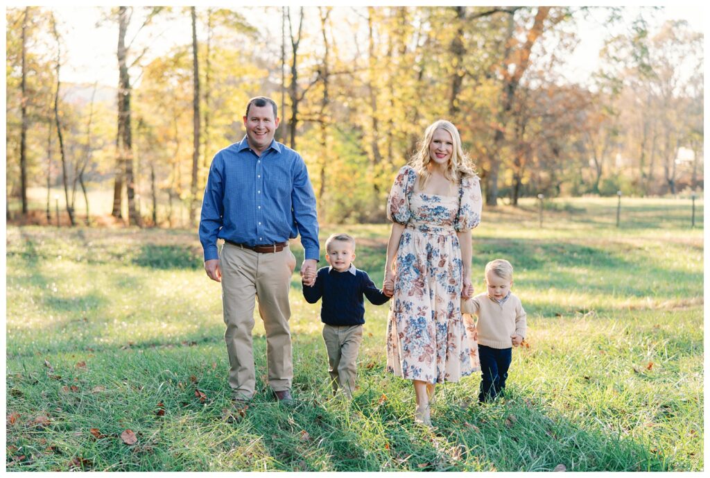 Atlanta fall mini session of parents and their children in a field of green grass lines by trees with yellow, red, and orange foliage by Grace Emily Photography.