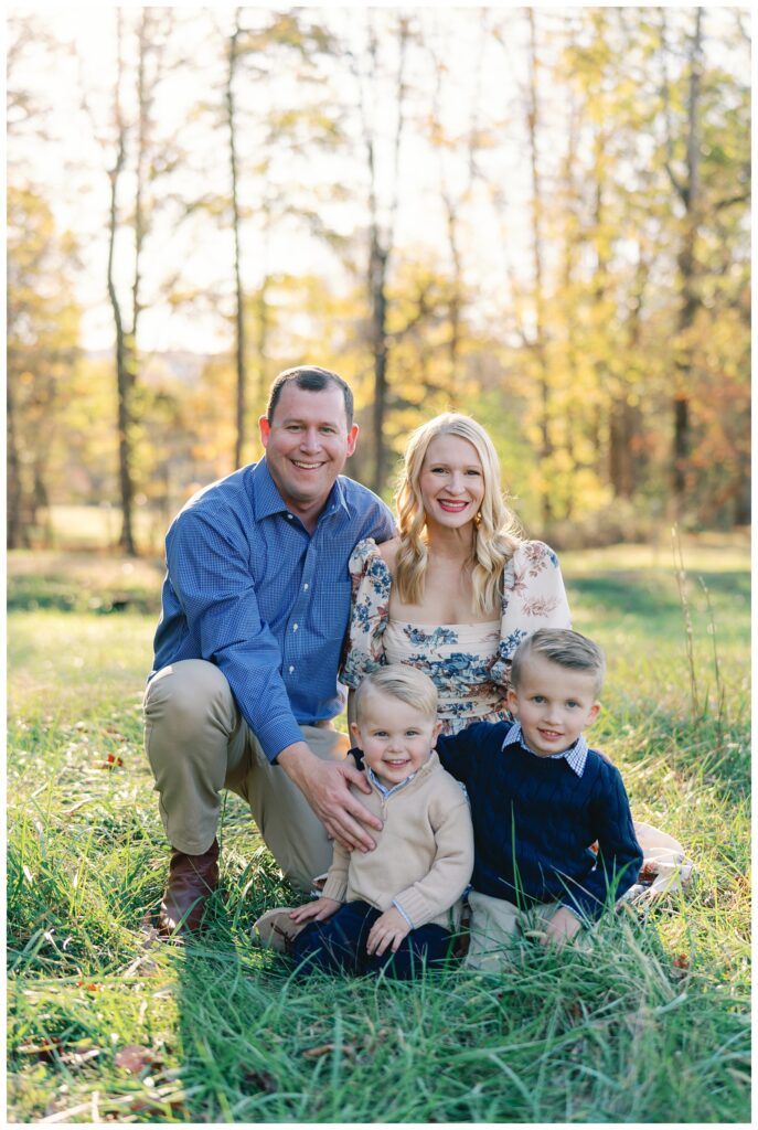 Atlanta fall mini session of a family in a field of green grass lines by trees with yellow, red, and orange foliage by Grace Emily Photography.