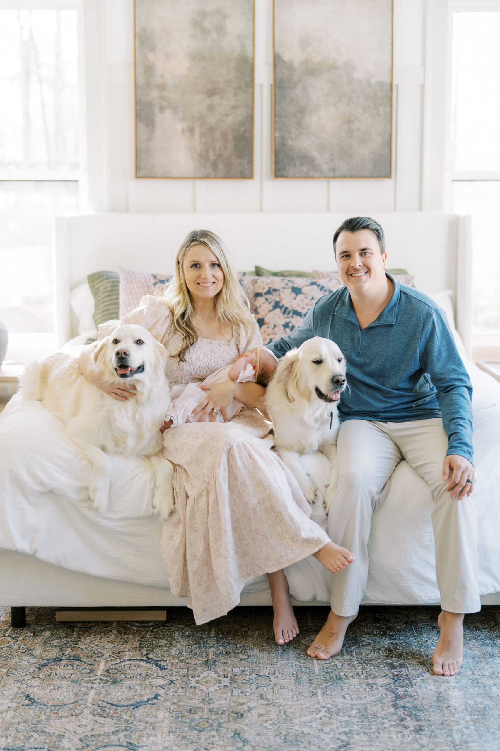 A mom holding a baby and dad sitting with their two golden retrievers